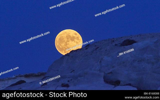 Telephoto shot, Large yellow full moon over rocks, sky midnight blue, Sarakiniko Bay, Milos Island, Cyclades, Greece, Europe