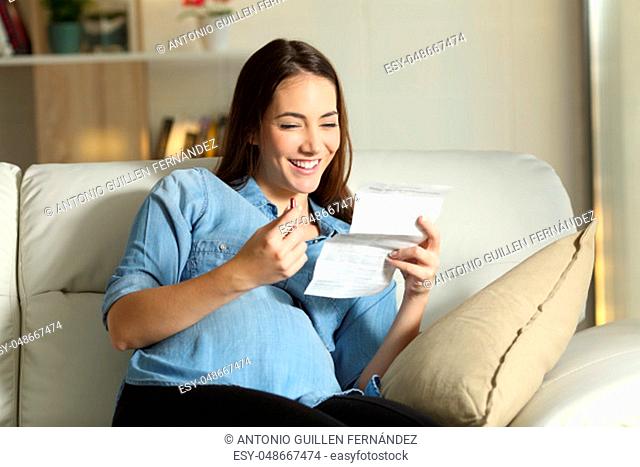 Happy pregnant lady reading a leaflet before take a pill sitting on a couch in the living room at home