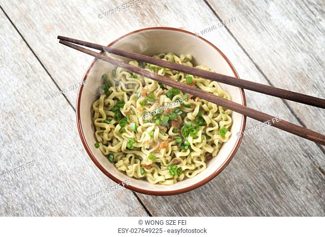 Top view bowl of cooked Asian dried noodles with chopsticks on wooden table