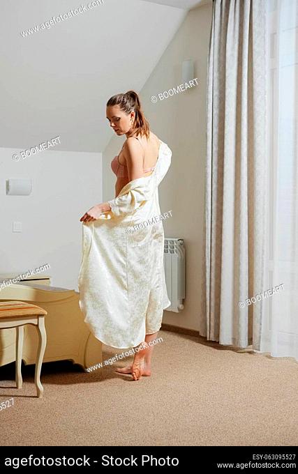 pretty young lady in bedroom taking off silk peignoir near the bed before go to sleep