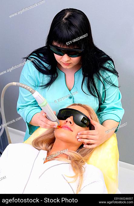 Beautiful young woman is getting facial mask at spa. She is lying and relaxing. Her eyes are closed with pleasure. The cosmetologist is applying cream on her...