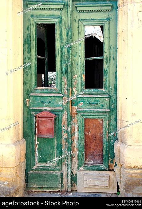 broken old double green doors in an abandoned derelict house with broken windows and faded peeling paint in a yellow stone frame