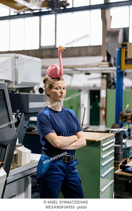 Young woman working as a skilled worker in a high tech company, balancing a pink flamingo on her head