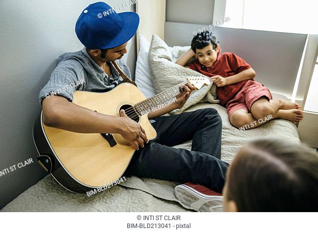 Mixed race boy watching brother playing guitar in bedroom