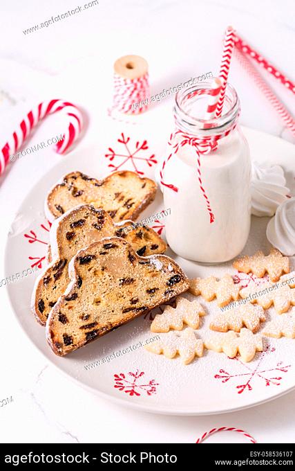 Bottle of milk with traditional Christmas stollen, small cookies and candy cane on white background. German Christmas bread
