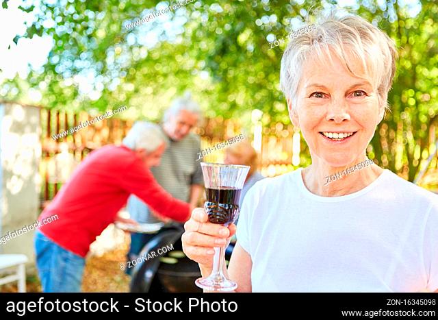 Fröhliche Seniorin mit einem Glas Wein auf einer Gartenparty im Sommer mit Freunden
