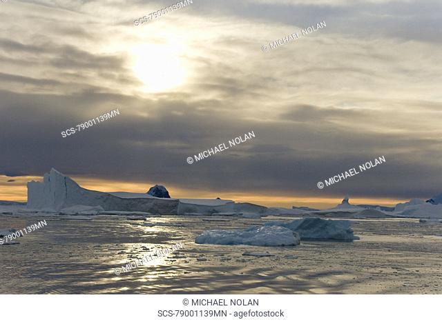 Sunset on snow capped mountains and icebergs surrounded in brash ice in Crystal Sound near the Antarctic Circle on the west side of the Antarctic Peninsula