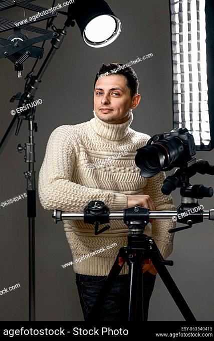 Professional handsome photographer with digital camera on tripod on gray background with lighting equipment