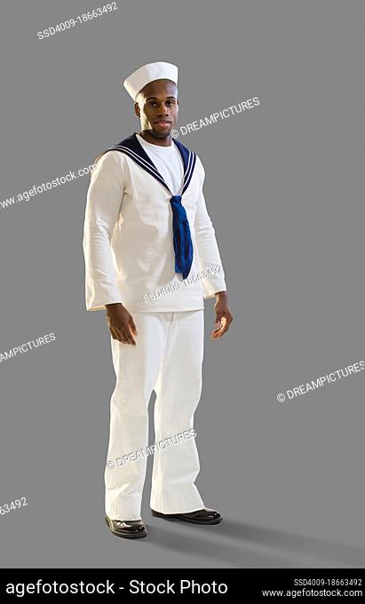 Full length portrait of a Black man dressed in a sailor Halloween costume looking at camera, on gray background