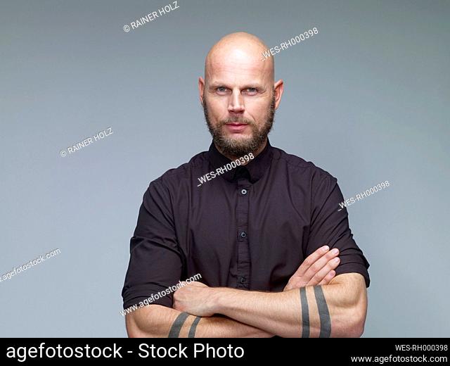 Portrait of man with bald and full beard in black in front of grey background