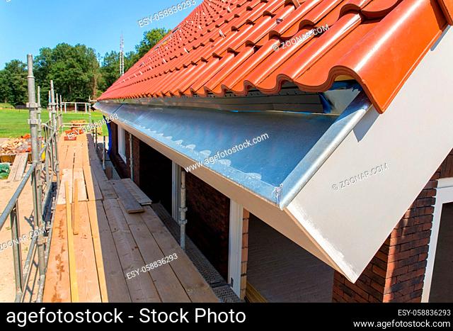Zinc rain gutter with roof tiles and scaffolding at new house
