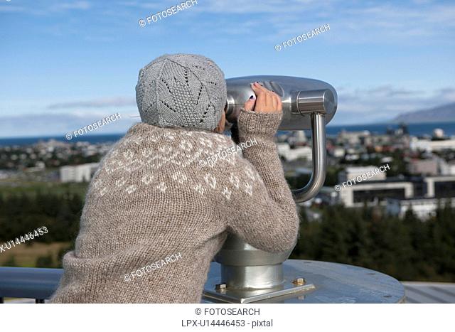 Young girl looking through binocular telescopic viewer at cityscape
