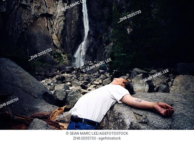 A man lying on his back with his arms spread under the foot of Bridevail Falls at Yosemite National Park in California, USA