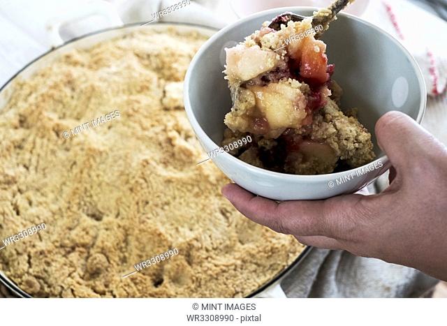 High angle close up of person holding bowl of freshly baked apple and blueberry crumble