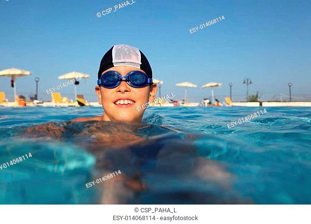 little boy with glasses for swimming and bathing cap, swim in pool. in background beach umbrellas. from the underwater package