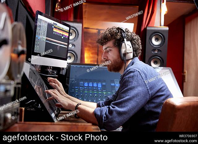 Man working in music studio using computer wearing head phones