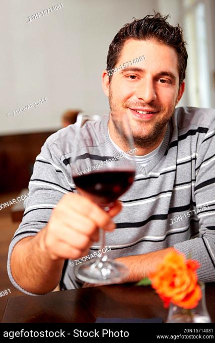 Mann prostet mit Glas Rotwein im Restaurant