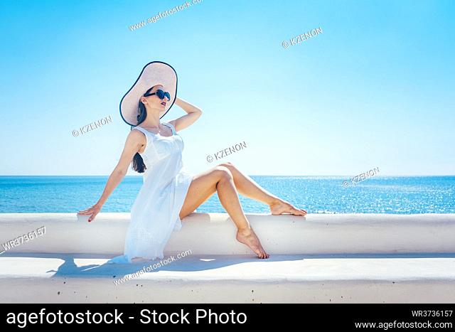 Woman sitting in the sun on a greek beach looking at the sea