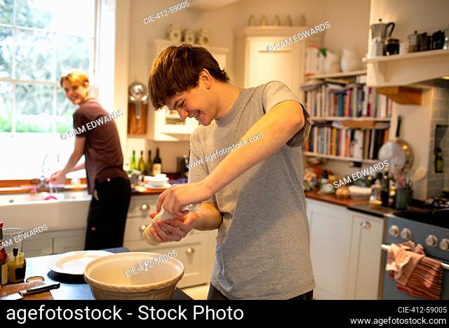 Happy teenage boy cooking with brother in kitchen