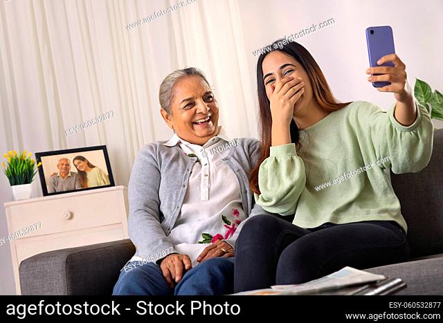 Grandmother and granddaughter taking selfie together at home