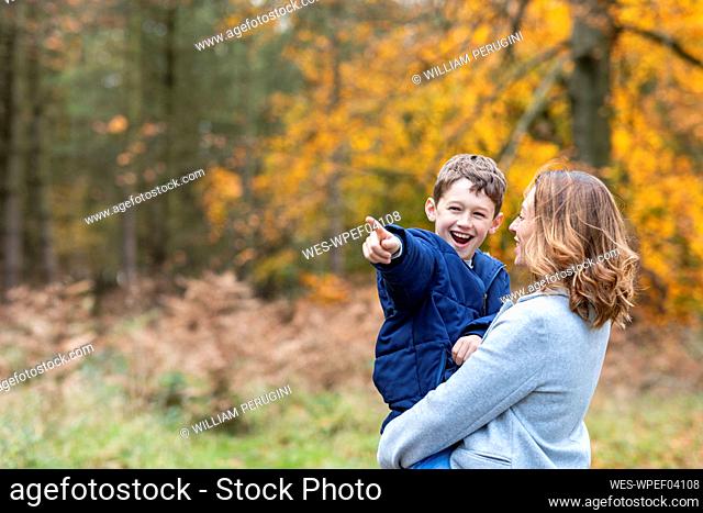 Smiling mother looking at son pointing while standing at forest