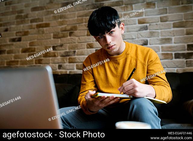 Man with laptop and book staring while sitting at cafe