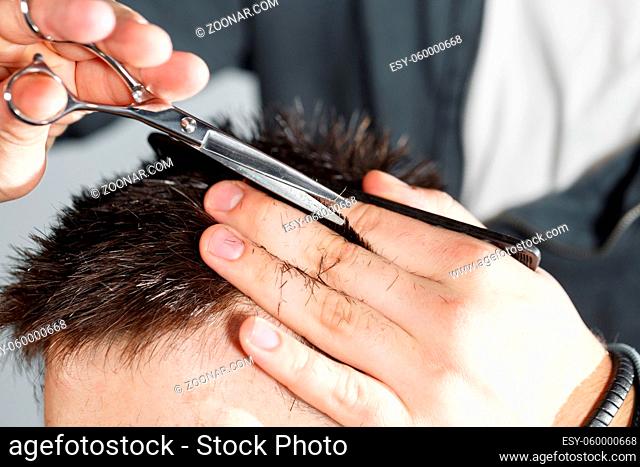 men's haircut with scissors at salon. Barber cuts the hair of the client with clipper at barbershop. Men's hairstyling and haircutting in a barber shop or hair...