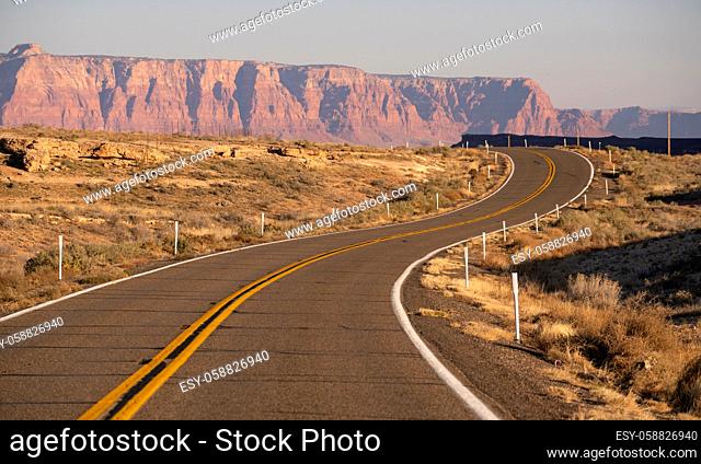 The sun hits golden rock buttes behind a rise and bend in the road desert southwest USA