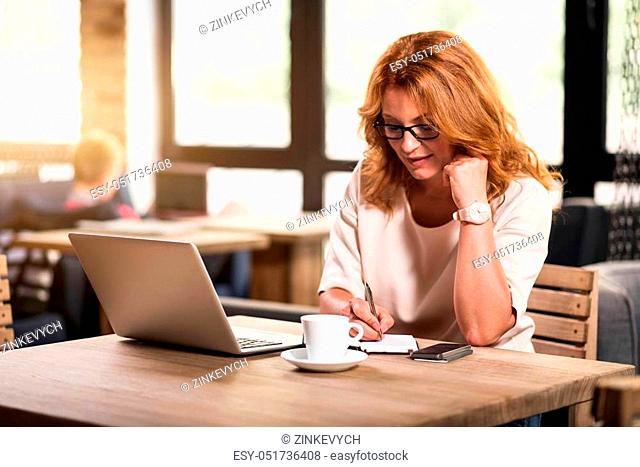 Wrapped in work. Confident business lady sitting at the table and making some notes while being in a cafe