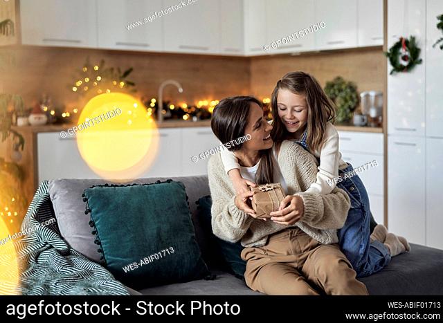 Smiling girl giving gift to mother sitting on sofa at home