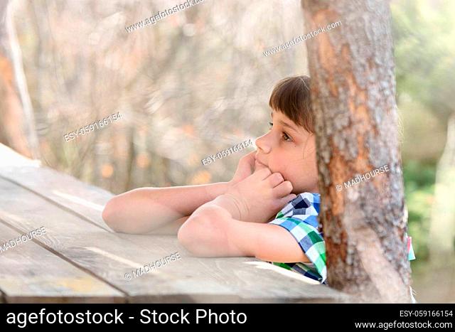 A ten-year-old girl sits at a wooden table in the forest and thinks