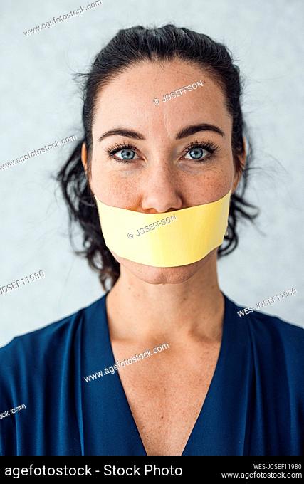 Woman with tape over mouth standing in front of gray wall