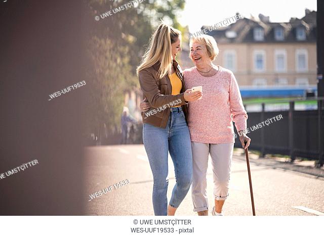Granddaughter and her grandmother walking on footbridge and using smartphone