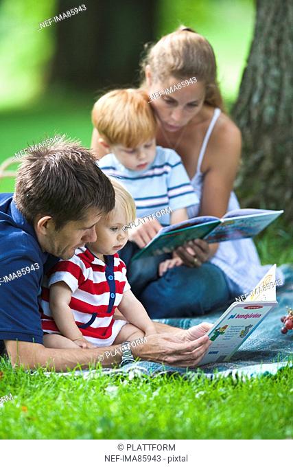Mid adult parents reading books to children during picnic