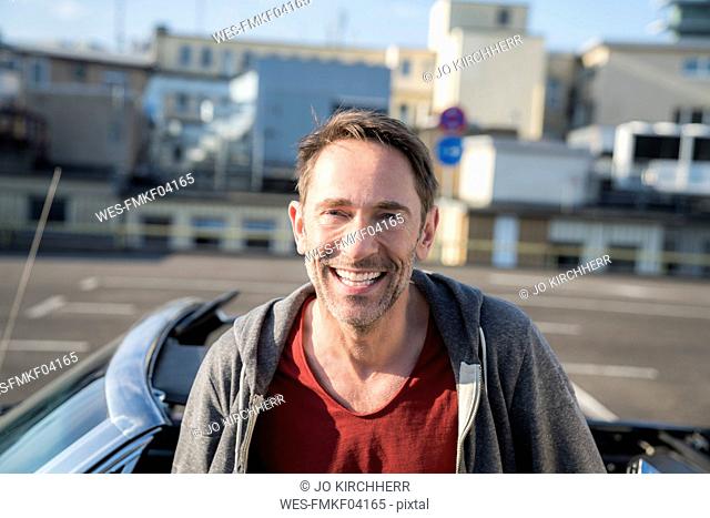 Portrait of laughing mature man with stubble in front of his sports car