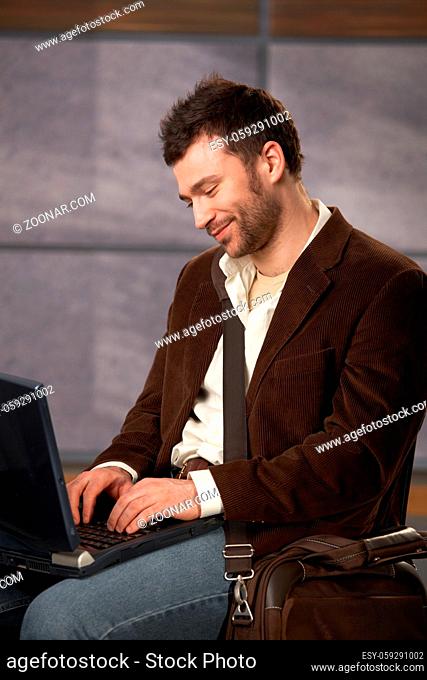 Smiling young office worker using laptop computer in office lobby