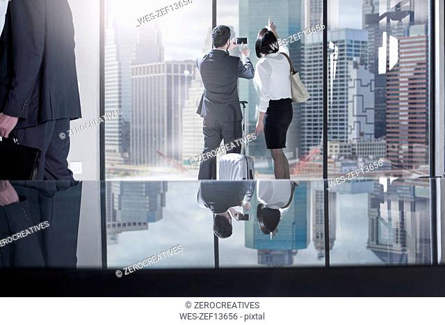 Businessman with rolling suitcase taking photos of city view in office