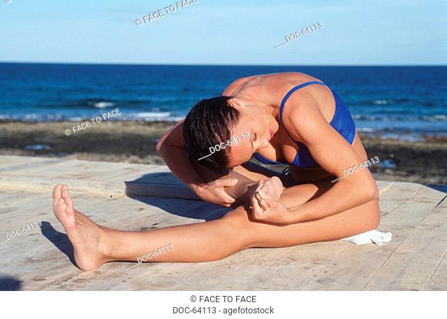 woman does doing sports on a platform at the sea, extension practice in the Seated