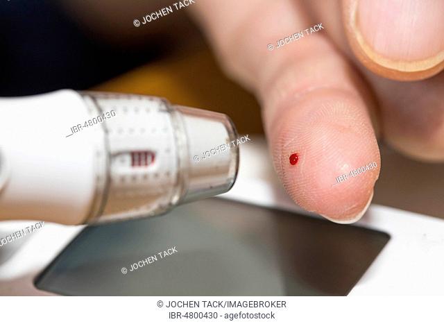 Diabetics taking a blood glucose test, with a lancing device a drop of blood is produced at the fingertip, Germany