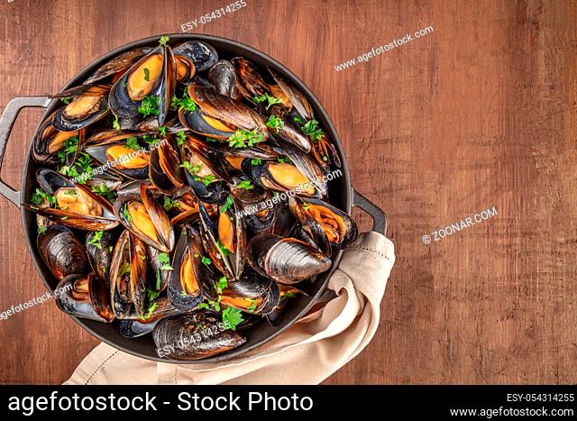 Marinara mussels, moules mariniere, in a large cooking pan, overhead shot on a dark rustic wooden background