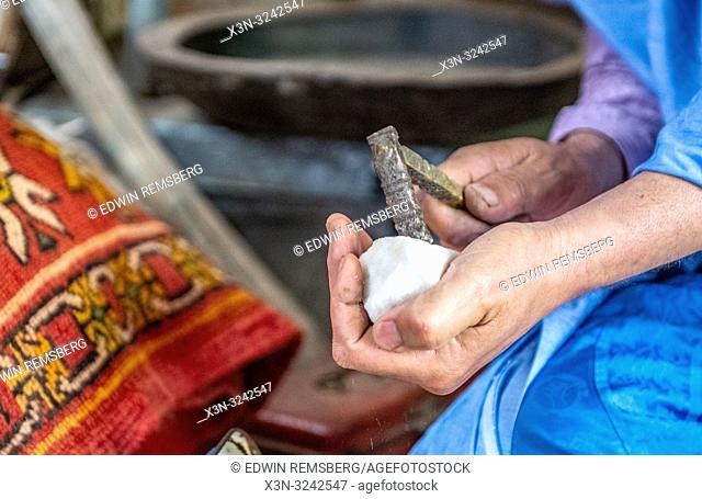 Berber man uses crude hammer to break off piece of sugar for traditional Moroccan tea ceremony, Tighmert Oasis, Morocco