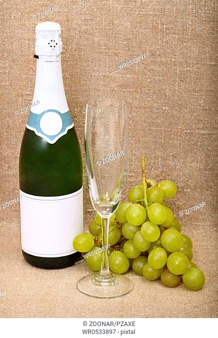Still-life from bottle of sparkling wine, empty glass and grapes