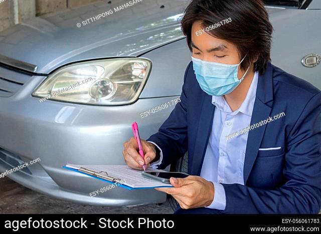 Sitting Asian Insurance Agent or Insurance Agency in Suit Wear Mask Checking Car Crash Data Report from Accident for Claim at Garage