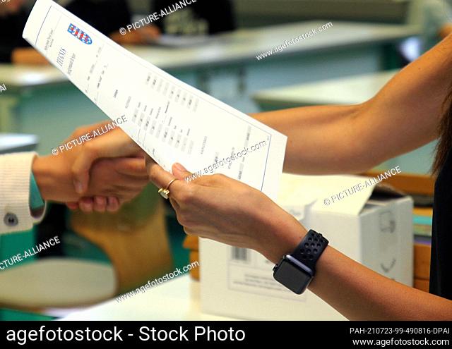 23 July 2021, Thuringia, Erfurt: A teacher at a high school stands in a classroom on the last day of school before summer vacation, report card in hand