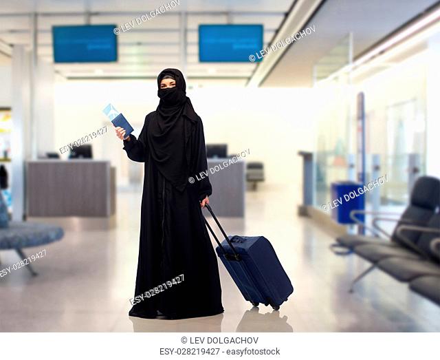travel, tourism, flight and people concept - muslim woman in hijab with airplane ticket, passport and carry-on bag over airport waiting room background