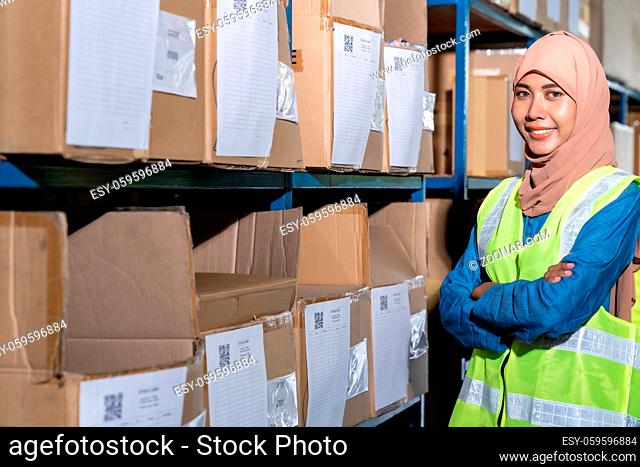 Portrait of Islam Muslim female warehouse worker crossed arm in front of product shelf with stock card in warehouse distribution environment