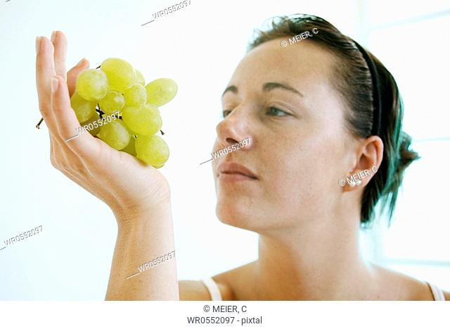 Young woman is looking at a bunch of grapes