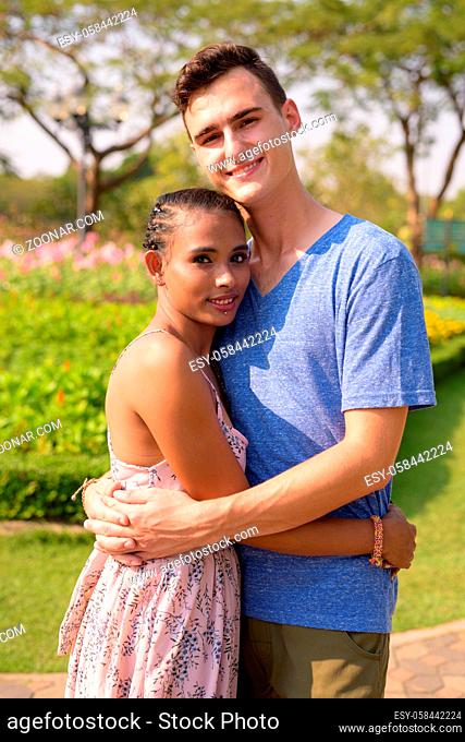 Portrait of young handsome man and young beautiful Asian woman relaxing together at the park