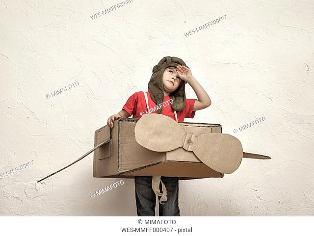 Little boy playing with pilot hat and cardboard box aeroplane