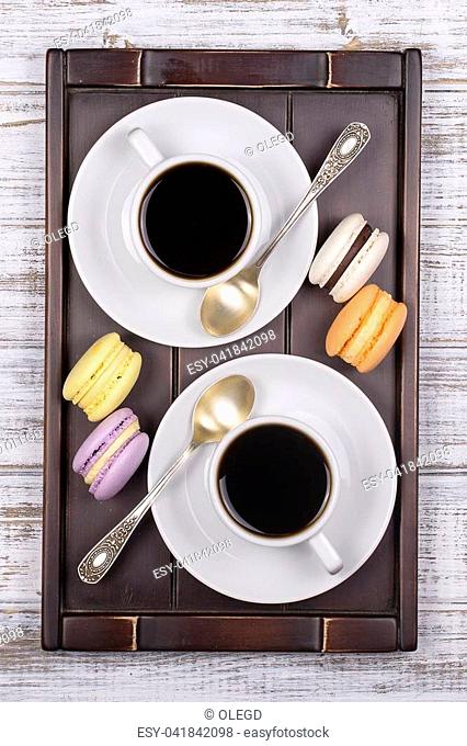 Two cups of coffee, spoon and macaron cakes on tray on white wooden table. Lifestyle concept. Close up. Top view